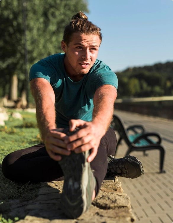 A man is seated on a bench, stretching his legs to improve flexibility and relieve tension.
