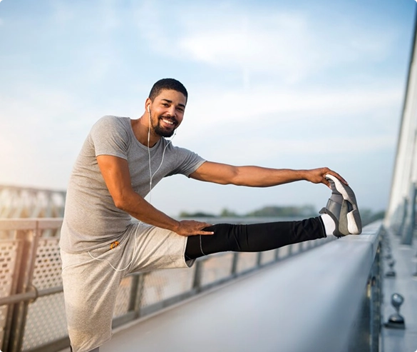 A man performs a leg stretch on a bridge, showcasing his athleticism with a view of the surroundings.