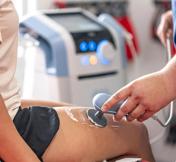 A healthcare professional uses an electric device to treat a patient's leg in a clinical setting.