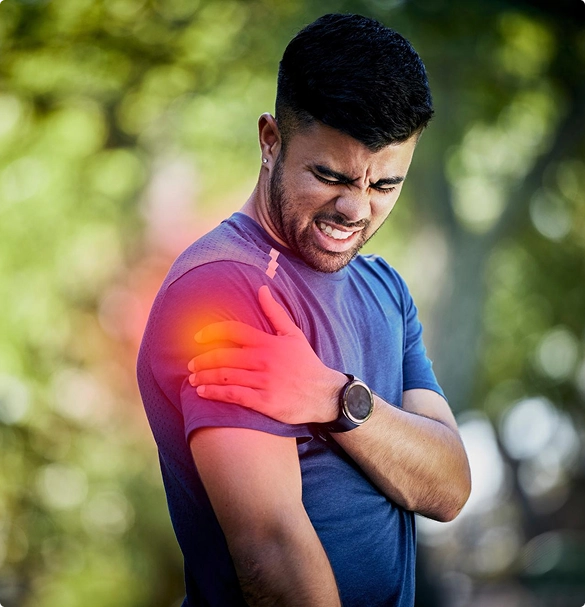 A man grimaces, holding his shoulder in discomfort, indicating pain in the joint area.