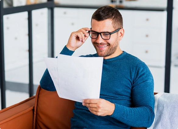 A man wearing glasses is focused on reading a document in a well-lit room.